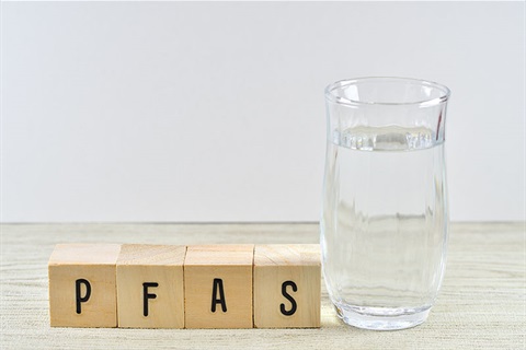 Words PFAS written with blocks next to glass of water